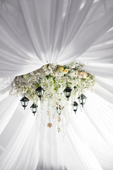 Chandelier made of roses and white flowers hangs under the light tent. decorative lights