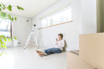 Schwangere Frau  sitzt auf dem Boden auf der Baustelle im Haus und telefoniert