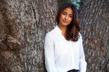 Beautiful calm relaxed at peace portrait of a mixed race woman standing in nature by tree bark