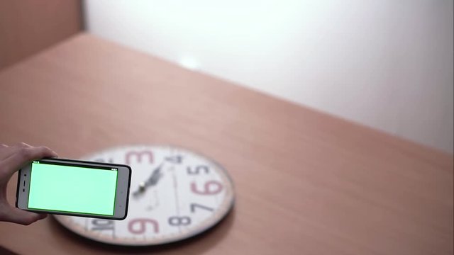 Smartphone scans wall-clock moving the hand to the right to the left along the clock with green screen