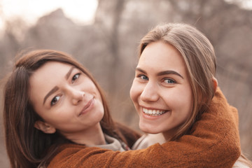 Two young women are hugging outdoors and laughing. Close up