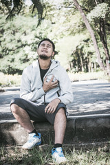 Obraz premium An Asian young man has a heart pain while exercising in a park.