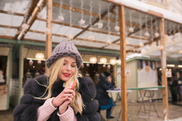 Wonderful blonde woman holding flavorous christmas gingerbread against light decoration at the Christmas fair in Kiev