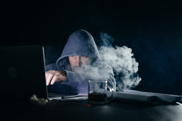 mysterious male hacker sits in the dark and smokes a hookah