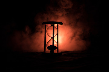Time concept. Silhouette of Hourglass clock and smoke on dark background with hot yellow orange red blue cold back lighting, or symbols of time