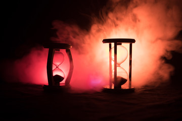 Time concept. Silhouette of Hourglass clock and smoke on dark background with hot yellow orange red blue cold back lighting, or symbols of time