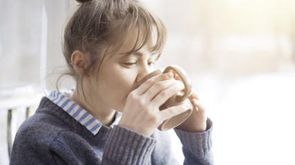 Beautiful woman wearing a gray sweater is enjoying her tea in a cafe and daydreaming. Portrait shot