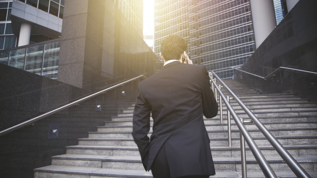 A Handsome Businessman Walking Up Stairs And Having Phone Conversation. Concept Of Business Success.