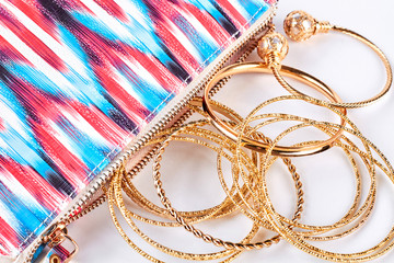 Close up of golden bangles and bag. Golden wrist bands and pink patterned cosmetics bag close up. Woman fashion accessory.
