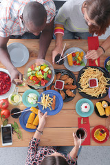 Top view of group of people having dinner together while sitting at wooden table. Food on the table. People eat fast food.