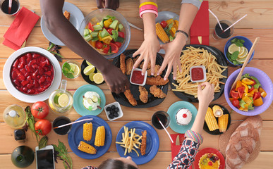 Top view of group of people having dinner together while sitting at wooden table. Food on the table. People eat fast food.
