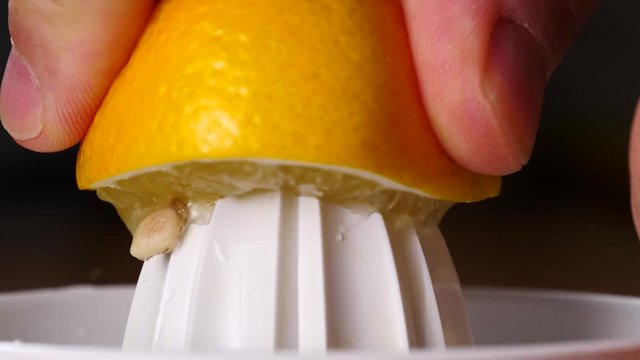 Male hand squeezing fresh lemon fruit using plastic juice squeezer. Making healthy citrus sour drink. Slow motion