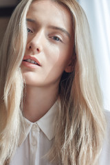 Portrait of a beautiful young woman with long loose blonde hair and chic makeup, wears white silk shirt. Adjusted with a touch of charming colors.