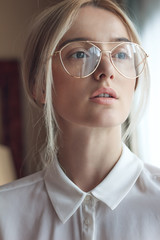 Portrait of a beautiful young blonde woman with chic makeup and big fashionable glasses, wears white silk shirt . Adjusted with a touch of charming colors.