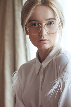 Portrait of a beautiful young blonde woman with chic makeup and big fashionable glasses, wears white silk shirt . Adjusted with a touch of charming colors.