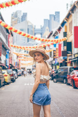 A beautiful young blonde woman exploring pretty part of Chinatown in Singapore. Hot weather in the colorful small urban downtown. She wears casual combination of clothes with a nice hat.