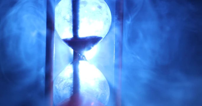 Time concept. Silhouette of Hourglass clock rotating in smoke on dark toned background, or symbols of time under smoke, the end