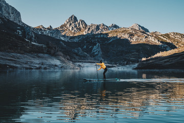a woman with yellow plumber paddle surfing on a lake in a snowy mountain landscape