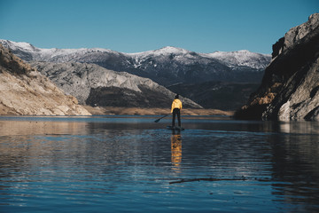 a woman with yellow plumber paddle surfing on a lake in a snowy mountain landscape