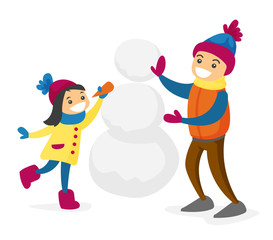 Happy caucasian white boy and girl building a snowman and playing in snow