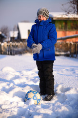 Schoolboy boy kicks the ball playing in winter football on the snow cover.