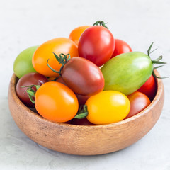 Small colorful cherry tomatoes in wooden bowl on a table, square format