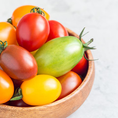 Small colorful cherry tomatoes in wooden bowl on a table, square