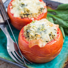 Baked tomatoes stuffed with quinoa and spinach topped with melted cheese on ceramic plate, square format