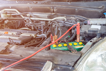 car battery clamped with black and red jumper cable to recharge the power