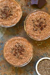 Chocolate chia seed pudding in glass bowls with chia seeds and chocolate shavings on top, photographed overhead on slate with natural light