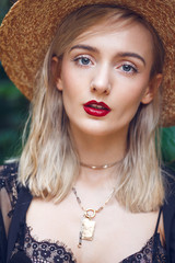 Close-up portrait of a gorgeous blonde woman with straight cut hairstyle and with straw hat, green mysterious eyes and sexy red lips. She wears fashionable black lace clothing and golden necklaces