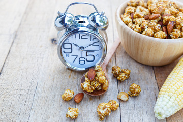 Popcorn caramel mix macadamia and almond taste and alarm clock on wood table with copy space.