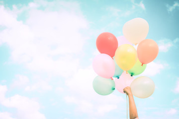 Fototapeta na wymiar Girl hand holding multicolor balloons done with a retro instagram filter effect, concept of happy birth day in summer and wedding honeymoon party, Vintage color tone style
