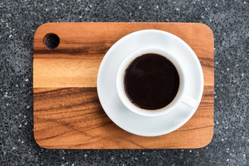 white cup of dark coffee on wooden plate on grey table, beverage
