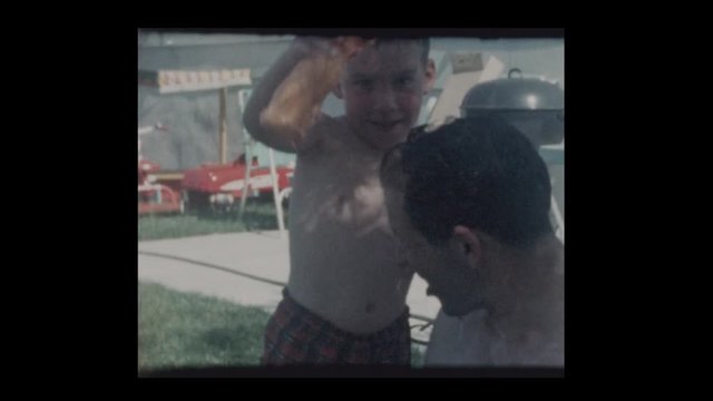 1964 Little boy pours water on dads head in kiddie pool