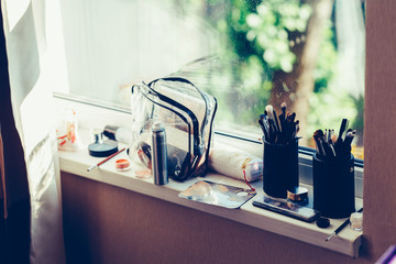 Cosmetics on the sill of the window. Makeup brush, palette, concealers. Vintage tonted photo.
