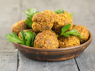 Freshly made falafel in a clay bowl with herbs on a dark wooden table.