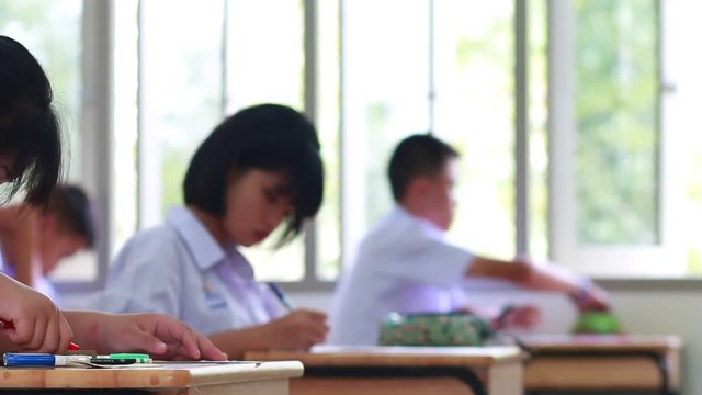 blurred of Female students wearing school uniform Concentrating on doing tests and taking exercises exams on wooden tables and chairs in secondary schools classroom Thailand, Educational concepts