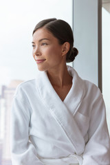 Fototapeta na wymiar Asian woman relaxing at luxury hotel spa wearing bathrobe looking at window portrait. Pampering comfort lifestyle at resort.