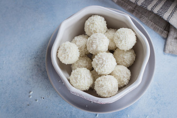 Coconut candies on gray plate on blue concrete table background. Top view, copy space