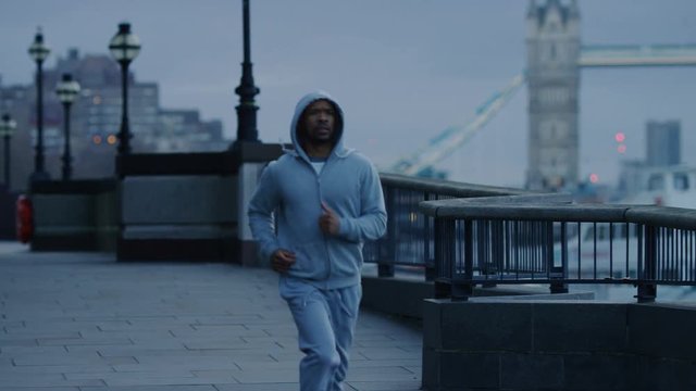 Hooded male jogger running by the river in early morning, in slow motion