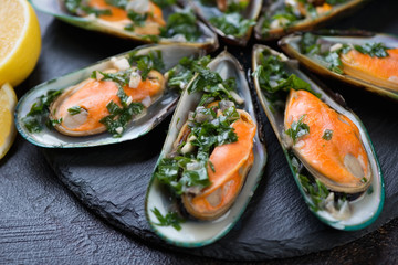 Close-up of boiled green mussels with parsley sauce on a stone slate, selective focus