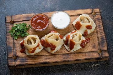 Rustic wooden serving tray with steamed meat dumplings manti, tomato sauce, sour cream and greens, studio shot