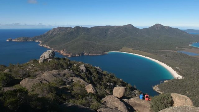 wide angle view of wineglass bay and two hikers from mt amos on the east coast of tasmania, australia