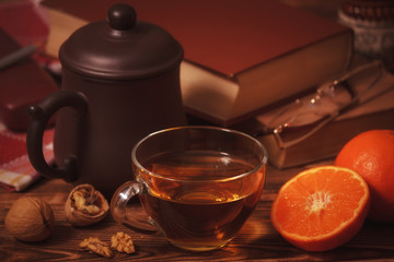 Cup of tea on wooden table with tangerines, walnuts and books