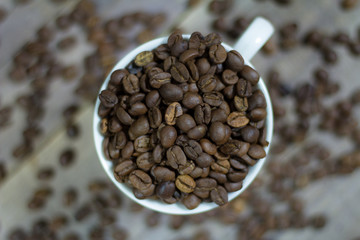 A cup full of coffee beans. Spilled coffee beans on a wooden table