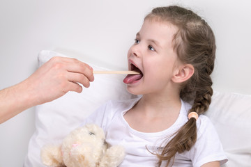 the child looks at the throat with a wooden stick, without getting out of bed