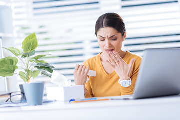 Sneeze. Beautiful young desperate woman feeling unwell while being ill and constantly sneezing when trying to work in her office
