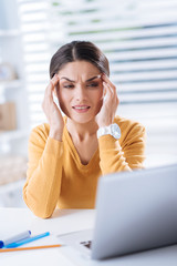 Migraine. Young exhausted employee sitting with her eyes closed and touching the forehead while...