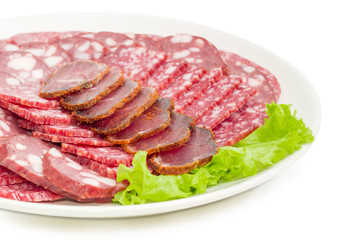 Sliced different meat products on lettuce on white dish closeup